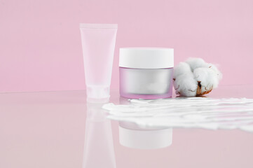 Cosmetics SPA branding mock-up. Matte cosmetic containers with cotton flowers, textured smears of white cream on pink background top view. Natural organic beauty product concept