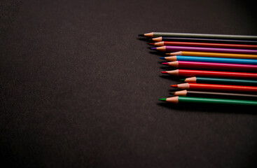 Colored pencils lie in a row on a black background. School supplies. Minimalistic style of photography.