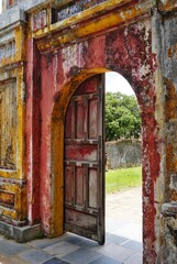 Fototapeta premium Ancient stone archway with crumbling red and yellow paint and half closed weathered wooden door