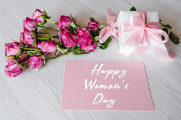 Composition of pink small roses, gift box, postcard on white wooden background. Happy Birthday. Holiday greeting card for Women's Day. Top view, flat lay.