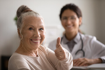 Head shot portrait smiling mature female patient showing thumb up, female therapist and senior man...