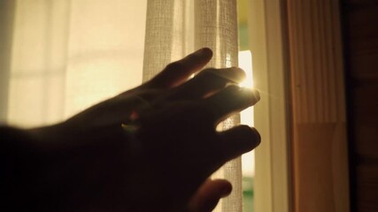 Slow motion hand moves towards a window curtain to reveal the sunlight outside. Sun shines through curtain during afternoon or early morning. Hand reaches slowly and dramatically. Hope and good energy