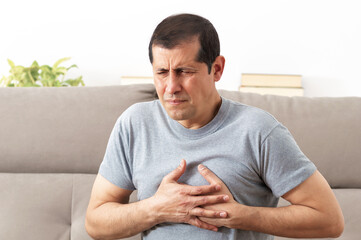 Cropped shot of an unrecognizable senior man holding his chest in pain sitting on a couch in the...