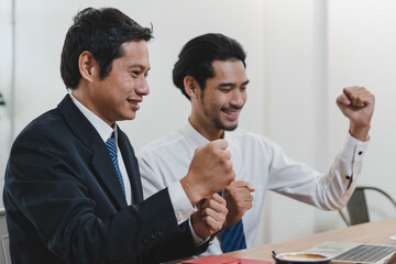Two happy asian business partners raise arm up to celebrating success achievement of company to win a deal with clients.