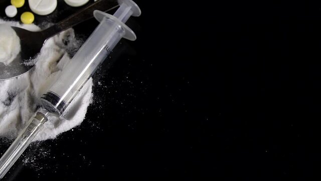 syringe and heroin and pills on a black background. Pills, ampoules with vaccine and drugs with syringe are rotating on black mirror background. 