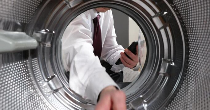 Broken washing machine. a man in a suit speaks through his smartphone about a broken washing machine. View From inside the washing machine