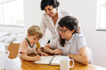 Female couple looking at their son scribbling in a book