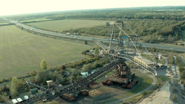 Aerial drone shot of a profitable open cast mining site with an industrial bucket wheel excavator next to a highway with driving cars passing by in Germany