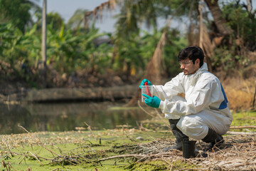 A man in full body protective suit collecting samples of water potentially contaminated by toxic material ,water quality monitoring concept ,ph checking on field.