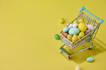 Fototapeta na wymiar Colorful Easter sweets in shopping basket on yellow background, holiday concept