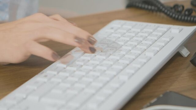 Woman types on keyboard in office. Stock footage. Woman is typing on computer keyboard with one hand. Woman works at computer in office