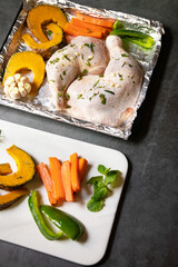 Chicken leg with spice and vegetables sliced in oven tray prepare for oven roast. Top view on black table background.