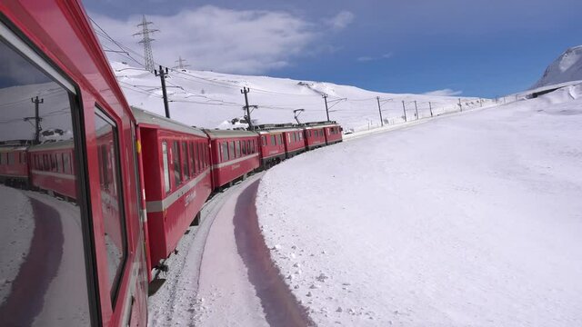Europe, Switzerland Alps , Poschiavo February 2021 - Live shot from the window  of the  Bernina Express, red train  pass in Ospizio Bernina station -  White lake ( lago bianco ) frozen 