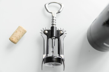 Metal corkscrew in a man's hand with a bottle of red wine on a background with a light white...