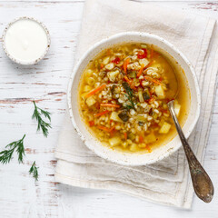 Thick hearty Pickle soup with vegetables (pickles, cucumbers, carrots, onions, potatoes, tomatoes) and pearl barley in a white plate on a wooden table. Rassolnik. Russian cuisine.  square picture