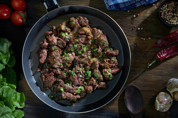 Stewed meat fried in a pan on a table with vegetables