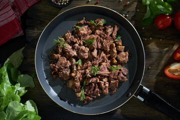 Stewed meat fried in a pan on a table with vegetables