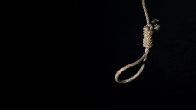 the gallows. the loop dangles. Rope noose with hangman knot in front of dark background