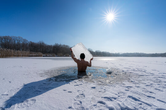 Young man holding an ice floe above his head while taking an ice bath