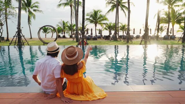 Young couple traveler relaxing and enjoying the sunset by a tropical resort pool while traveling for summer vacation