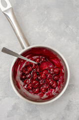 Cherry cooked with sugar and starch in a saucepan to make chocolate roll cake Black forest on a gray concrete background. Recipe step by step. Top view.