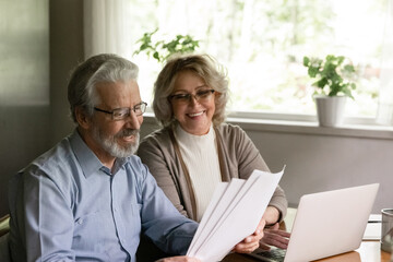Fototapeta premium Excited elder family pensioner couple read and check financial document, calculate profit, saving income from investment. OAP Senior man and 50s woman do monthly paperwork, make utility payment online