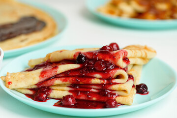 blini pancakes with red berry jam close-up on a blue plate on a light background . traditional...
