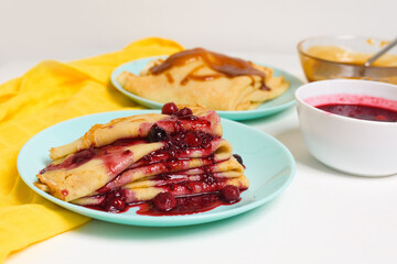 blini pancakes with red berry jam close-up on a blue plate on a light background . traditional...