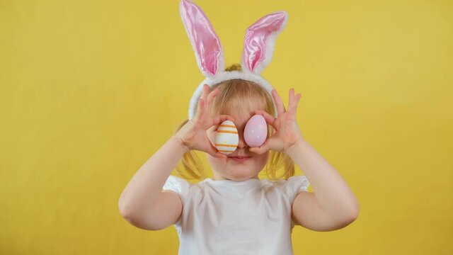 Portrait of cheerful blond little kid girl playing with easter egg on yellow background.