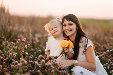 Happy mother and daughters in the park. Beauty nature scene with family outdoor lifestyle. Happy family relaxing together on the green grass, smiling and looking at the camera.