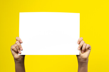 Hands holding blank white paper board poster placard on yellow background