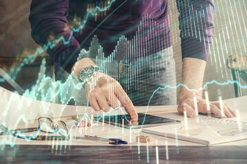 Double exposure of man's hands holding and using a digital device and forex graph drawing. Financial market concept.