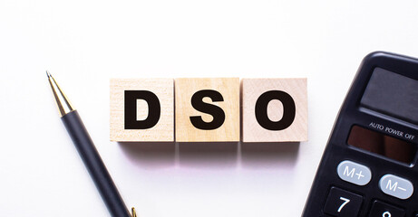 The word DSO Days Sales Outstanding is written on wooden cubes between a pen and a calculator on a light background.