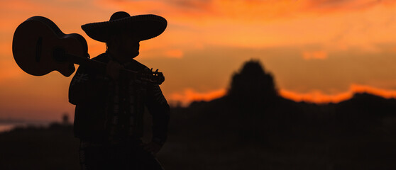 Silhouette of a Mexican musician with a guitar. Mariachi on the beach at sunset.