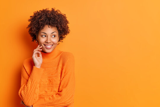 Studio shot of pleasant looking thoughtful smiling ethnic woman  concentrated aside expresses positive emotions wears casual sweater stands  against vivid orange background with copy space for text Stock Photo |  Adobe Stock