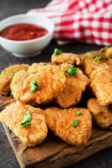 Homemade chicken nuggets with herbs and ketchup on a wooden board