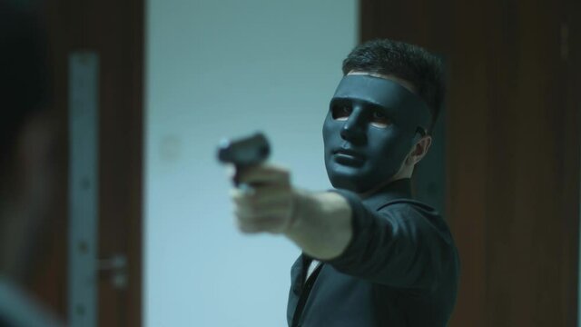 a charismatic handsome man in a mask dances and talks with a gun