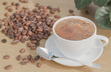 White Coffee cup and coffee beans on wood table with plant and white brick wall background.