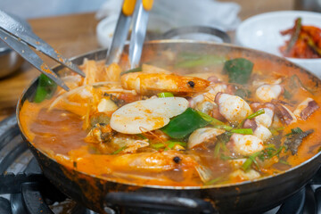 The spicy Korean-style abalone seafood soup is boiling, so the seafood is being cut with food scissors to eat.