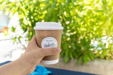 Woman hand holding delivered paper cup of hot coffee on green plants background.