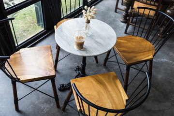 Iced coffee with straw and vase of decoration plant on the marble tale in cafe.