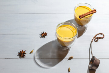 Two glasses of golden milk on a wooden gray background, with space and a copper ladle. Yellow milk drink with added spices