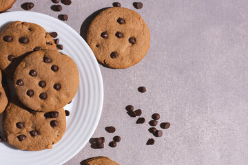 Homemade chocolate chip cookies on a small plate with gray background, top view. Hard and contrasting shadows