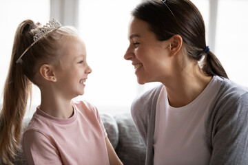 Happy mom expressing love to little daughter girl wearing princess diadem. Mother talking to child, smiling, laughing, having fun with cute little kid at home. Family bonding, relationship concept © fizkes