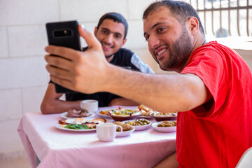 Muslim man and his friend are taking selfie and eating breakfast