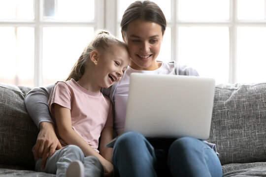 Happy mum and cute gen Z kid watching funny movie on laptop at home. Smiling mother and daughter girl using pc device, talking to family via video call, shopping online, playing games on internet