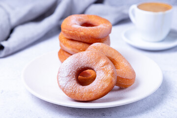Donuts with powdered sugar and a cup of coffee. Traditional donuts in the shape of a ring fried in oil. Unhealthy but tasty food. Close-up, light background.