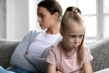 Annoyed upset quiet mother and kid sit on couch separately after arguing and quarrel. Offended school daughter girl ignoring mom. Silent parent and child going through conflict and behavior problem