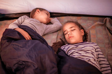 Kids sleeping in the camping tent during family local getaway. Children in the sunrise light, overnight in the wild nature. Healthy lifestyle, green local tourism and vacations, campsite. Soft focus