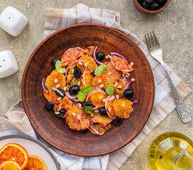 A healthy salad of sliced bloody oranges, purple onions, olives and pine nuts with olive oil dressing on a brown plate against an gray concrete background. Vegan recipes.